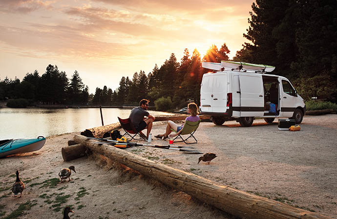 Couple setting next to a lake wit ha Mercedes-Benz Sprinter van.