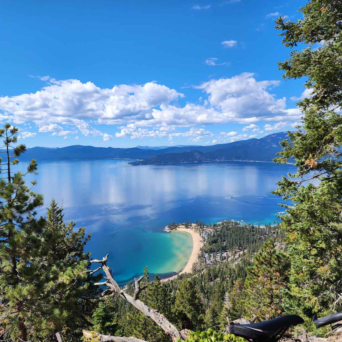 bikerumor pic of the day a photo of a view out over a clear blue lake with the seat of a bicycle in the bottom right corner, the sky is blue and had fluffy white clouds on the horizon.