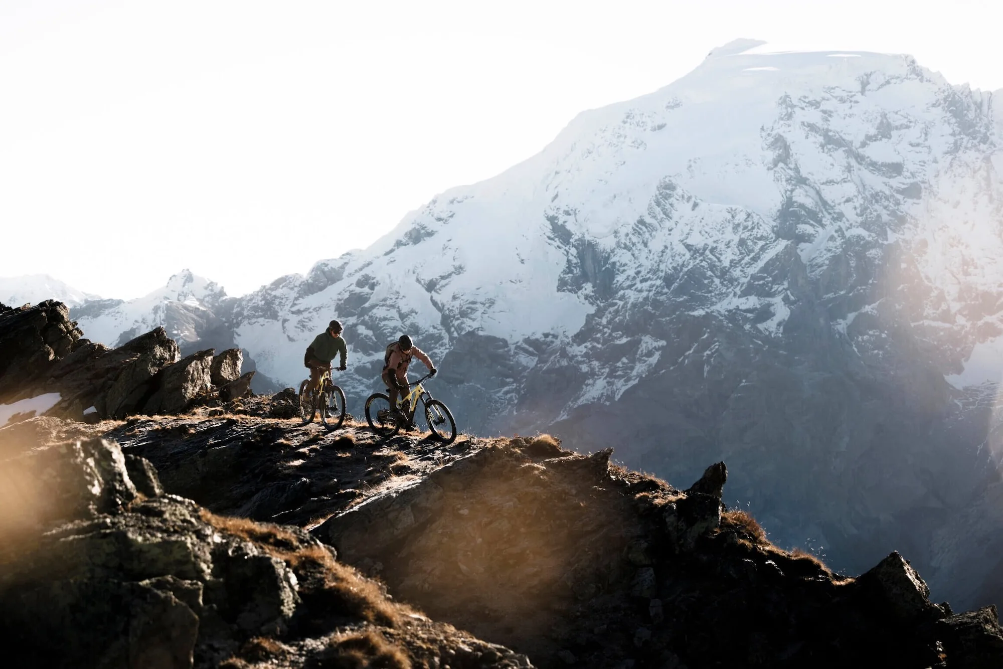 Two mountain bikers riding on a scenic rideline with snowy mountain in the background