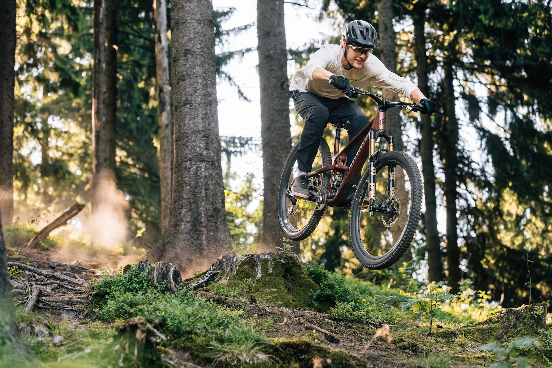 A rider on the new Propain Hugene bike hitting a small stump jump in the forest.