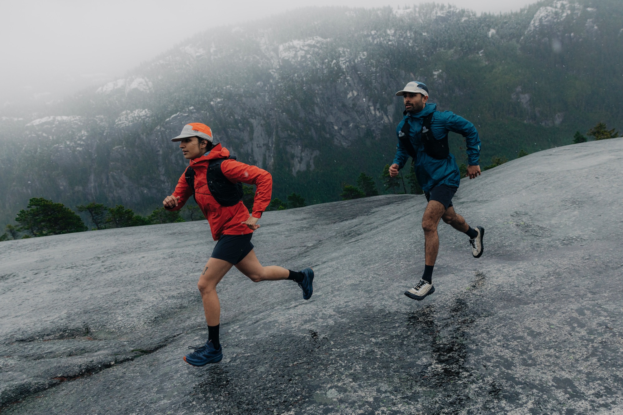 two people running across a large rock slab while wearing the 7Mesh Guardian Jackets