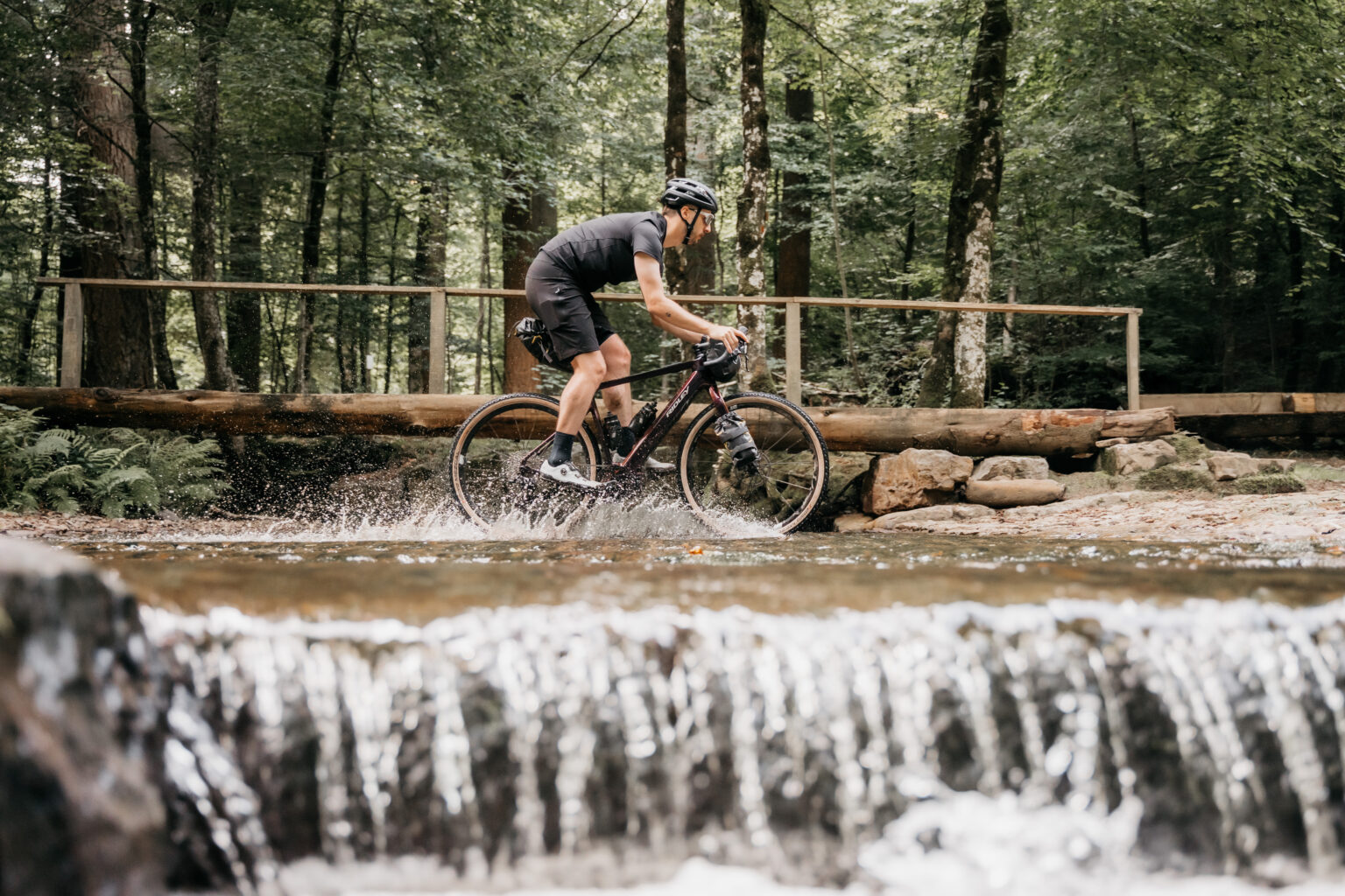 a man riding the E-Kanzo across a stream ahead of a small waterfall