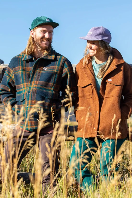 a couple wearing the Hungry Horse Jacket and leaning against a fence