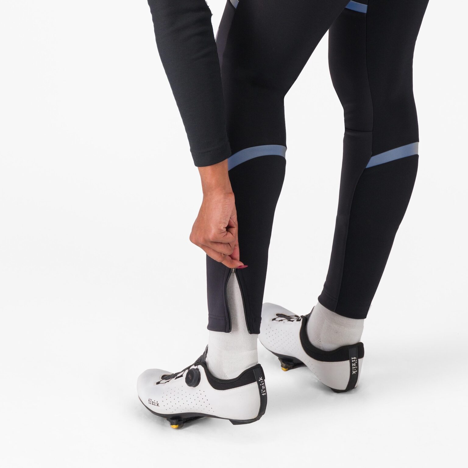 studio image of a woman zipping the ankle zip on the Polare bibtights.