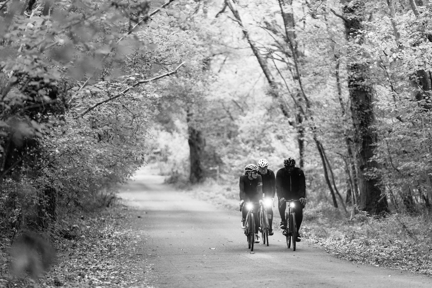 three riders on a smooth gravel road riding with lights on.