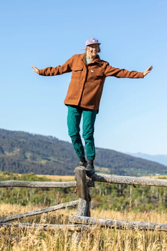 a woman wearing the Hungry Horse Jacket balancing on a fence