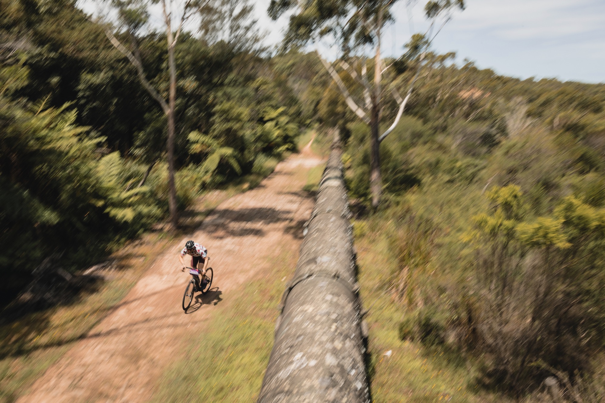 a man riding the Lombard E down a dirt road/path next to a large pipe.