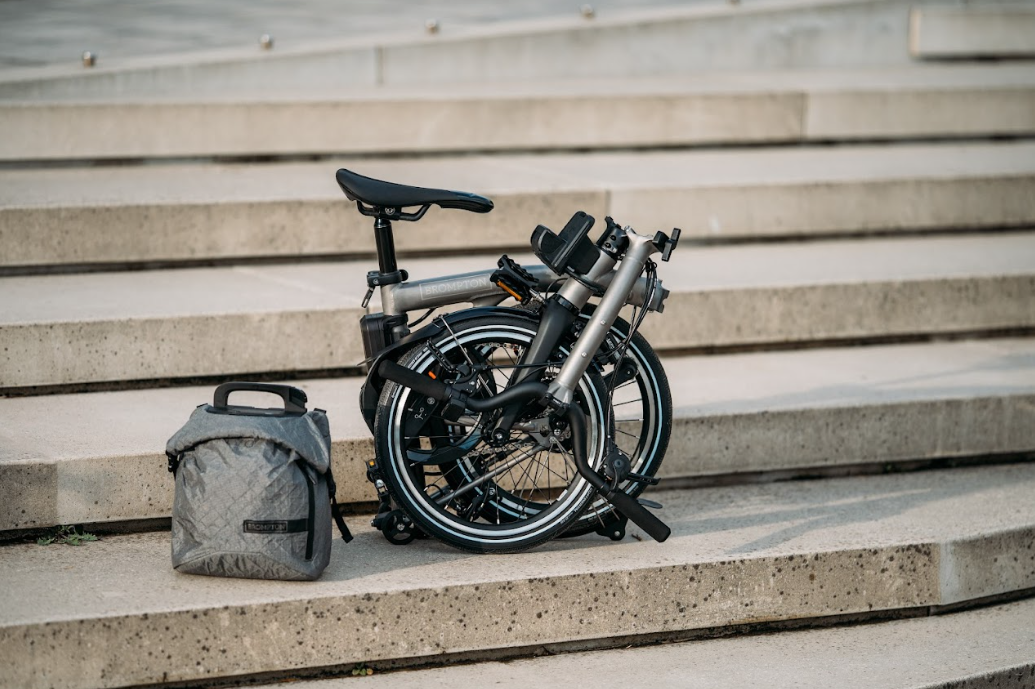 a Brompton folding bike with the new e-Motiq system folded up on some steps