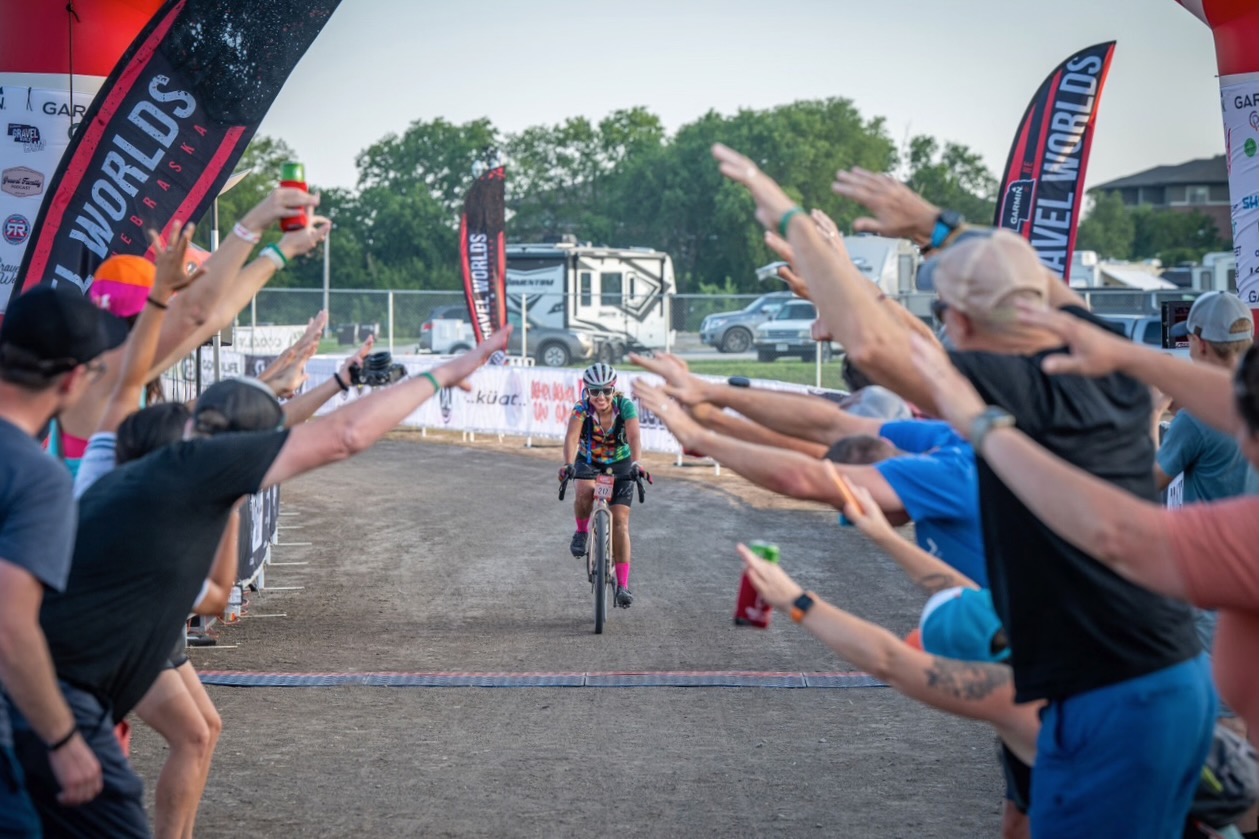 A rider crossing the finish line at Gravel Worlds with people sheering them on.