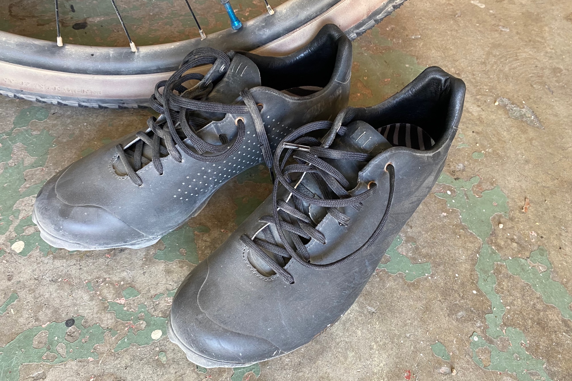 the giro empire XC shoes sitting on the floor next to a gravel bike wheel.