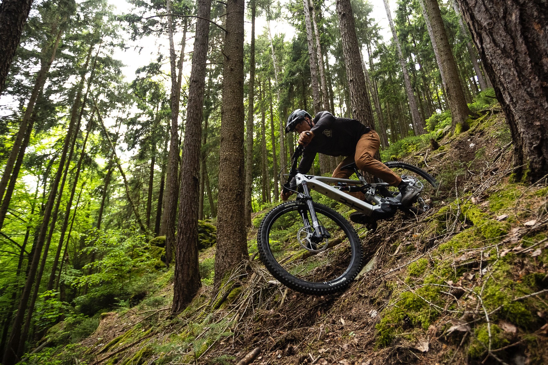 a person riding the YT Decoy X down a steep trail in a forest.
