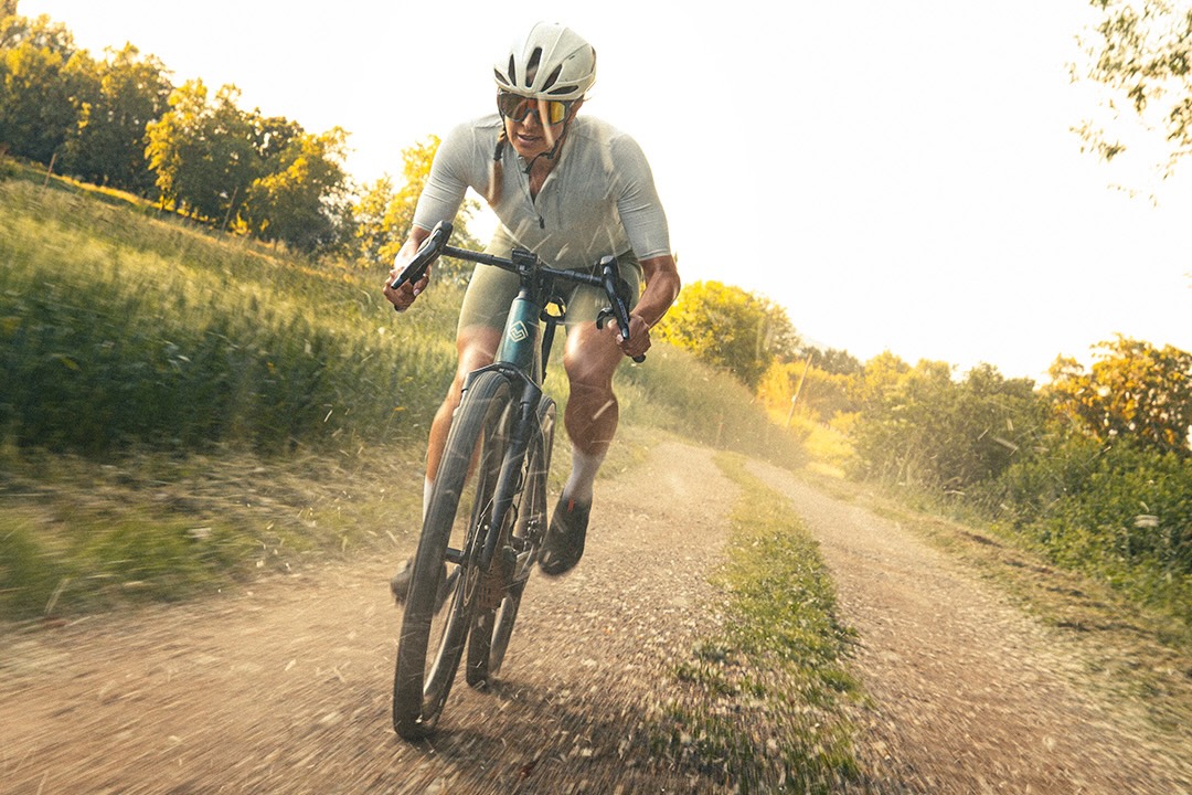a woman riding the Megamo Along e-gravel bike on a gravel road.