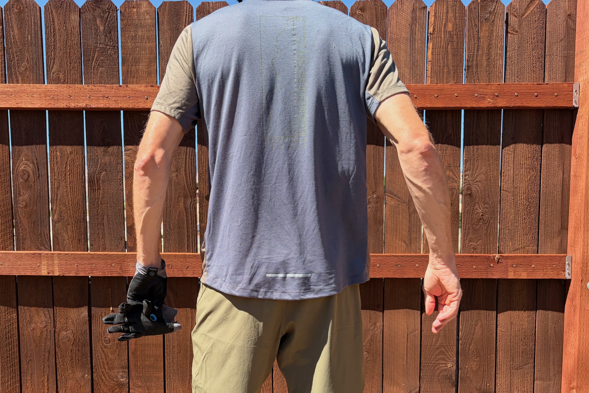wearing the slickrock tech T standing by a fence, viewed from the back